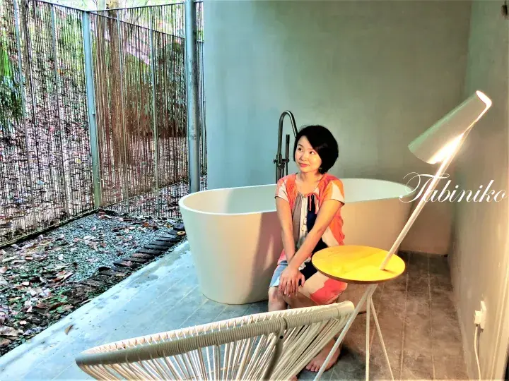 Woman sitting beside a modern freestanding bathtub in a minimalist bathroom with a view of a lush garden.