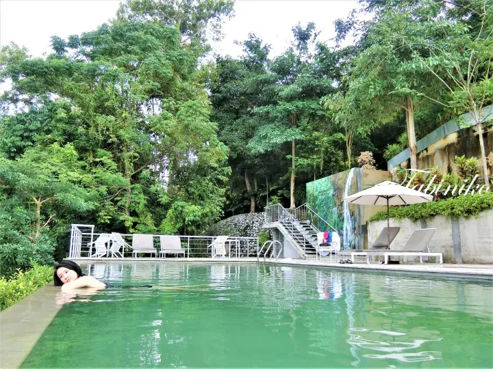Woman relaxing in a resort swimming pool surrounded by lush greenery and tropical trees.