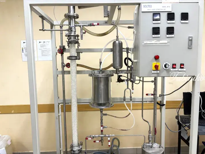Industrial solid-liquid extraction unit with stainless steel columns, pipes, and control panel in a laboratory setting.