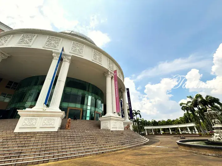 Grand white building with curved colonnade and glass facade at a Malaysian university campus.