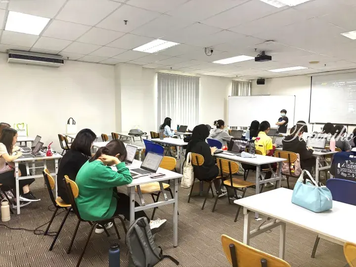 Students attending a lecture in a modern classroom with laptops and a projector screen.