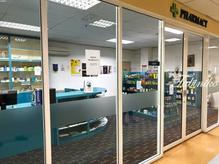 Mock pharmacy teaching facility with blue counters and medicine shelves for student training.