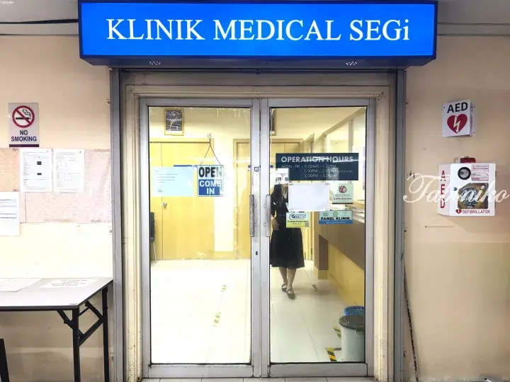 Entrance to Klinik Medical Segi with blue sign, glass doors, and AED box on the wall.