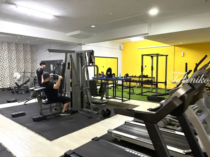 A man exercises on a weight machine in a gym with yellow walls, treadmills, and mirrors.
