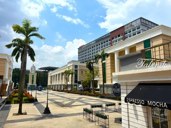 Modern campus plaza with palm trees, a clock tower, and a coffee shop awning under a blue sky.