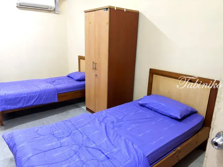 A clean guest room with two single beds featuring purple bedding and a wooden wardrobe.