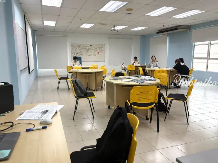Students studying at round tables in a bright, modern classroom with yellow chairs and whiteboards.