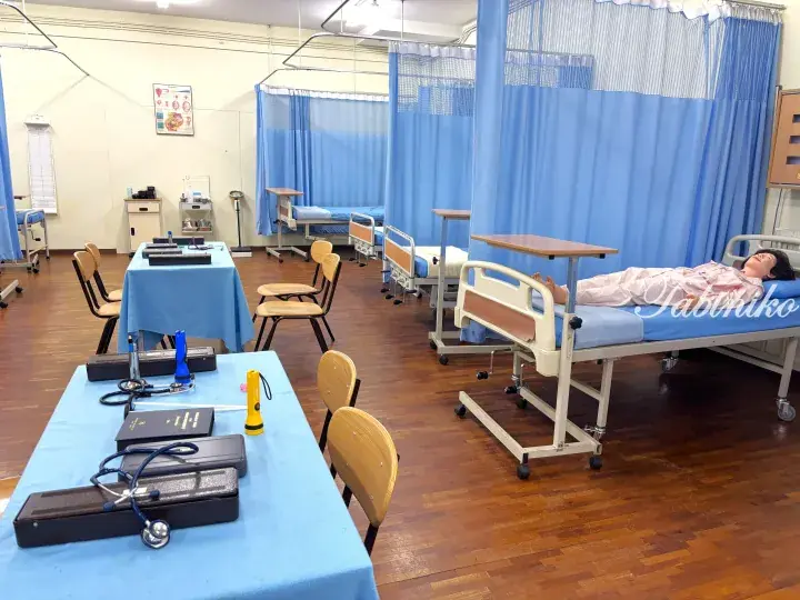 Hospital ward with patient beds, blue curtains, and medical equipment on tables in a clinical setting.