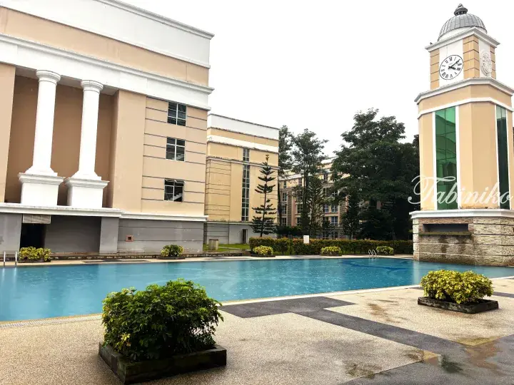 Swimming pool with beige buildings and clock tower at Tabiniko Resort in Malaysia.