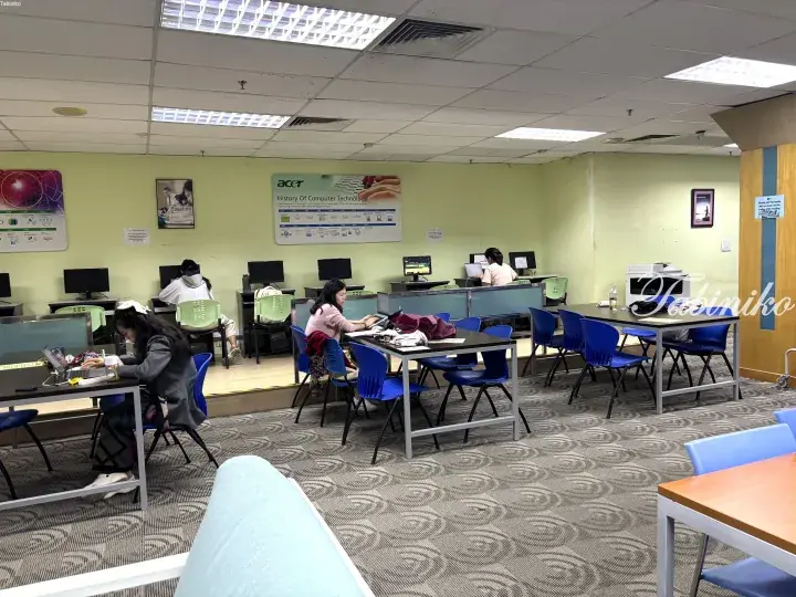 Students studying at desks in a modern library computer lab with Acer history poster on the wall.