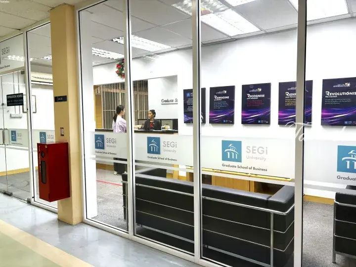 Glass entrance to SEGi University Graduate School of Business with posters and reception desk inside.