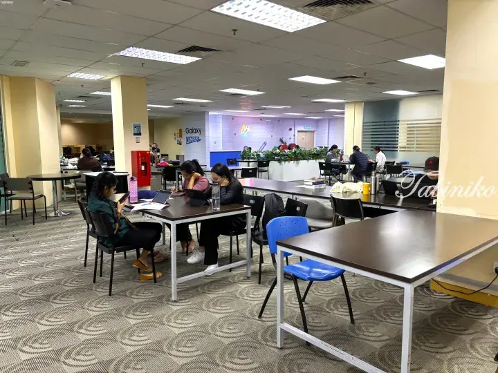 Students studying at tables in the Galaxy Campus library with modern furniture and bright lighting.