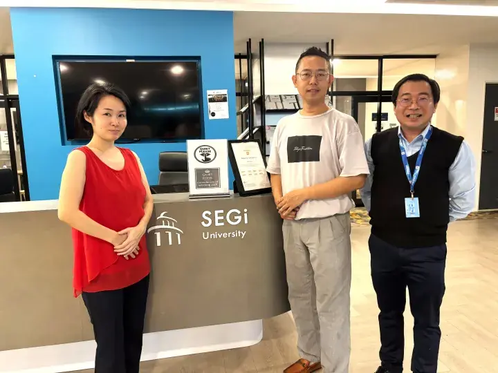 Three people standing at the reception desk of SEGi University in Malaysia.