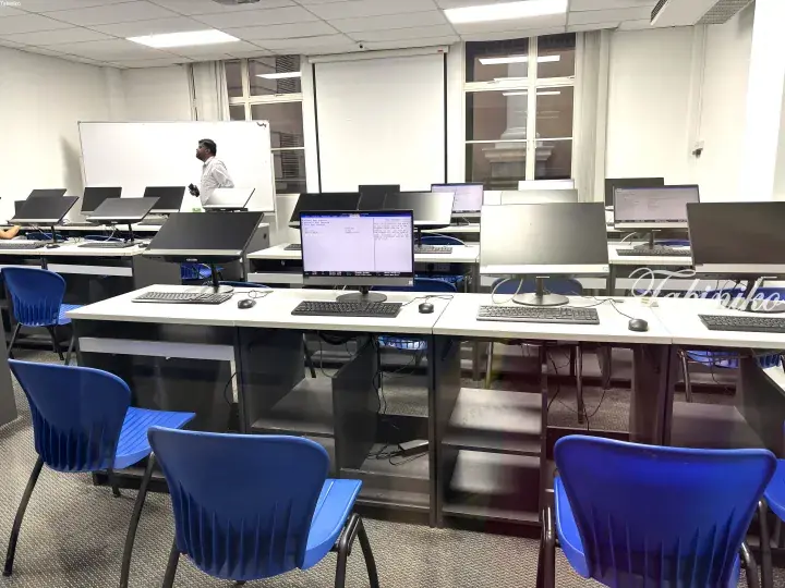 Computer lab with Lenovo monitors showing BIOS setup and a man standing near a whiteboard.