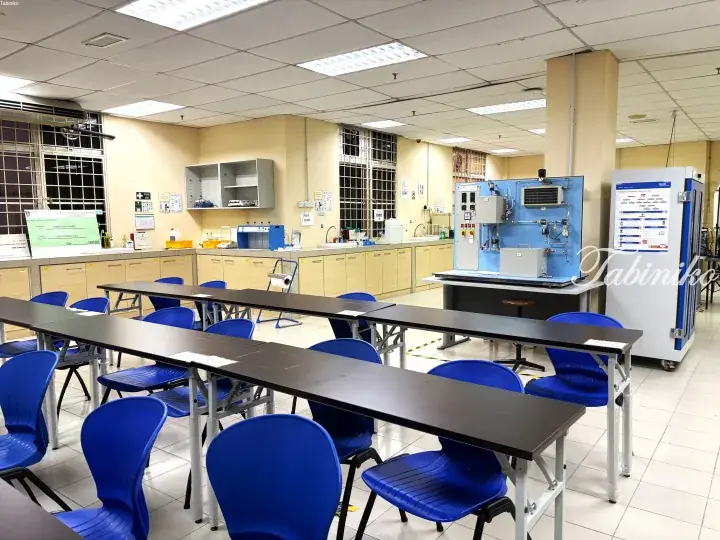 Modern laboratory classroom with blue chairs, long tables, and chemical engineering equipment.