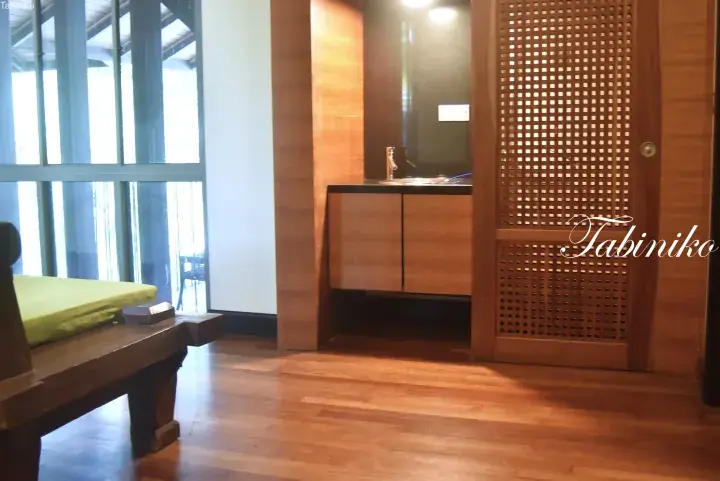 Spacious wooden floor interior with a green cushioned bench, sink area, and lattice door in a modern Malaysian property.