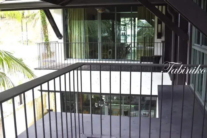 View from a balcony at a tropical resort showing glass doors, railings, and lush palm trees.