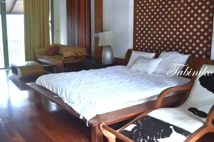 Spacious bedroom with wooden bed frame, white bedding, cowhide chair, and lattice headboard in a tropical villa.