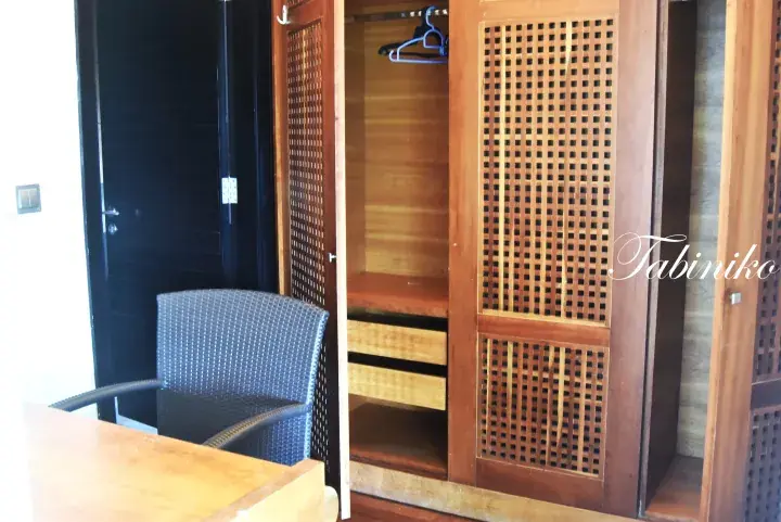 Open wooden wardrobe with lattice doors and drawers, next to a dark woven chair in a modern room.