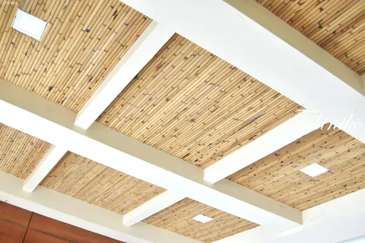 Close-up of a ceiling featuring bamboo matting panels framed by white beams and recessed lighting.