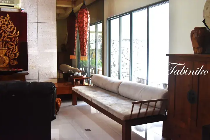 Spacious villa interior with wooden furniture, decorative lanterns, and large windows overlooking a garden.
