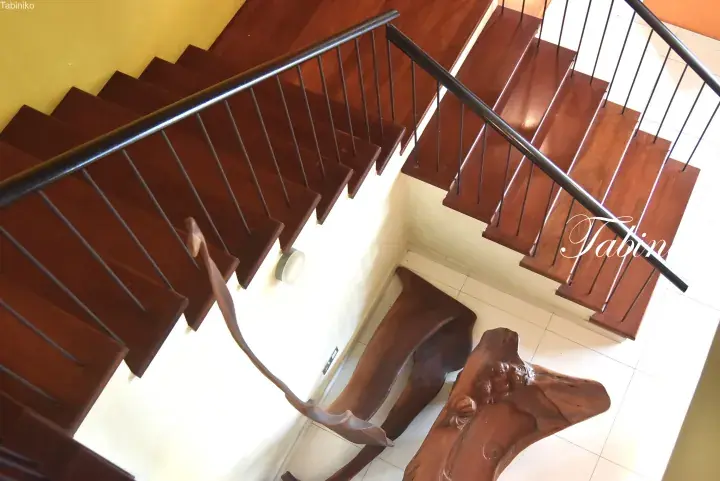 Wooden staircase with black railings and a carved wooden sculpture on the tiled floor below.