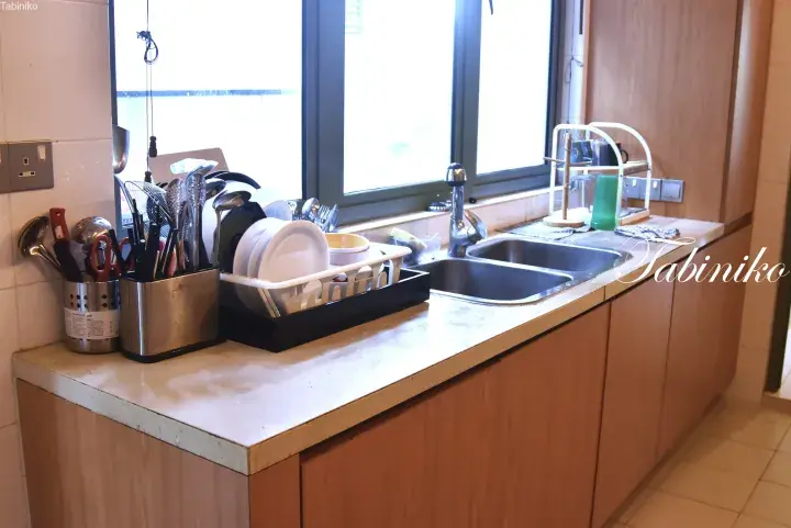Modern kitchen sink area with wooden cabinets, dish rack, and utensils near a bright window.