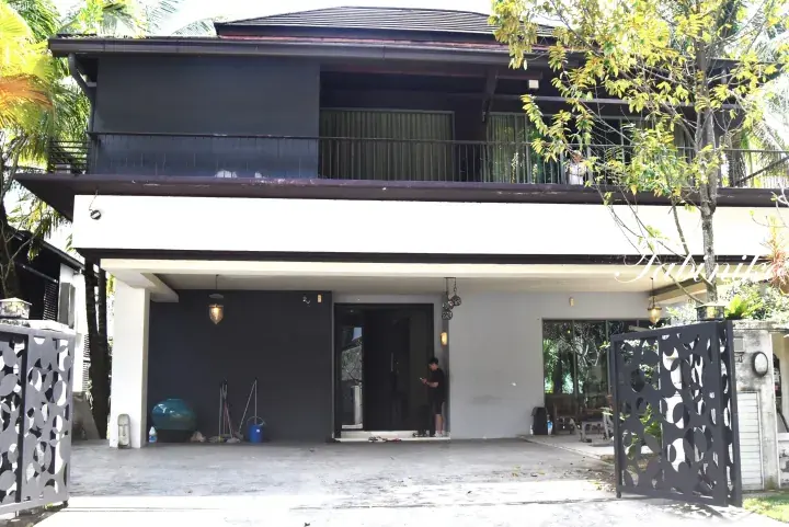 Modern two-story house with dark grey and white exterior, balcony, and decorative metal gate in tropical setting