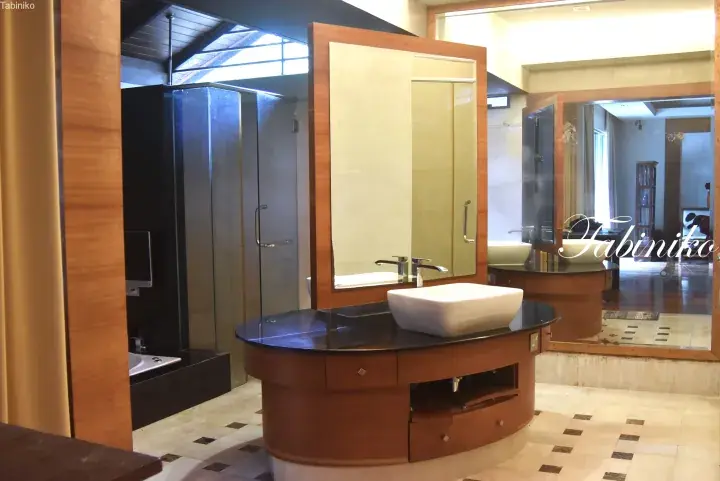 Modern bathroom with a curved wooden vanity, white vessel sink, and glass shower enclosure.