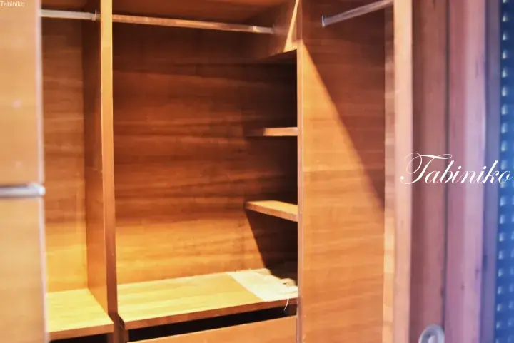 Interior view of a wooden wardrobe with shelves and hanging rods, featuring a Tabiniko watermark.