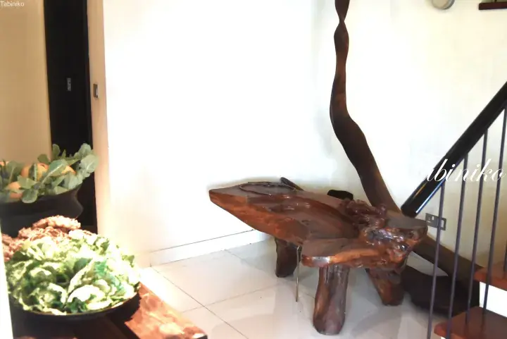 Unique hand-carved wooden table with a tall sculptural element, displayed in a bright property lobby near a staircase.