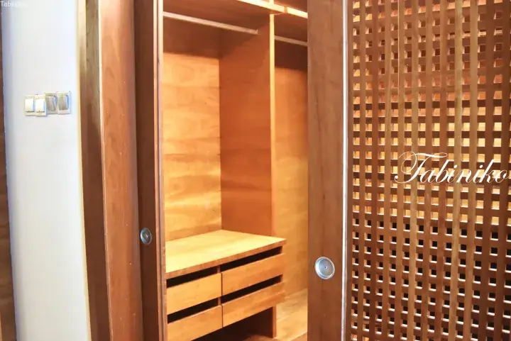Interior of a wooden walk-in closet with lattice doors, drawers, and hanging space.