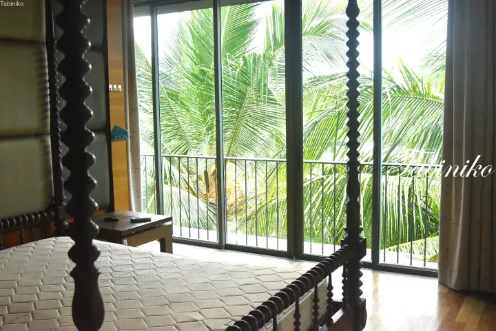Bedroom with a four-poster bed overlooking lush tropical palm trees through a balcony door.
