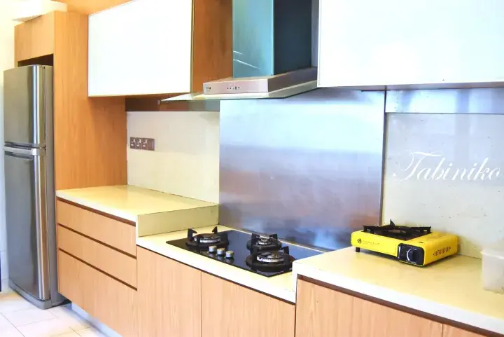 Modern kitchen with wooden cabinets, stainless steel fridge, built-in gas stove, and portable burner.
