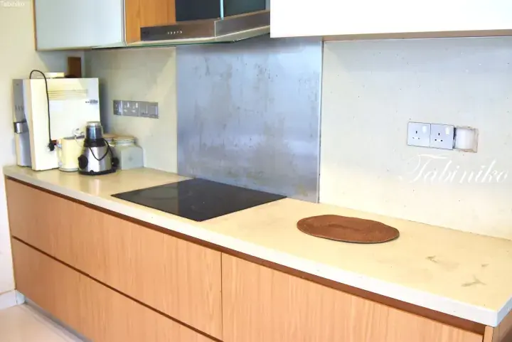 Modern kitchen with wooden cabinets, induction cooktop, and stainless steel backsplash in a Malaysian apartment.