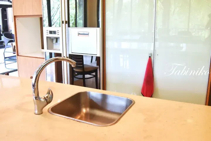 Modern kitchen sink with chrome faucet on beige countertop, featuring a water dispenser and frosted glass partition.