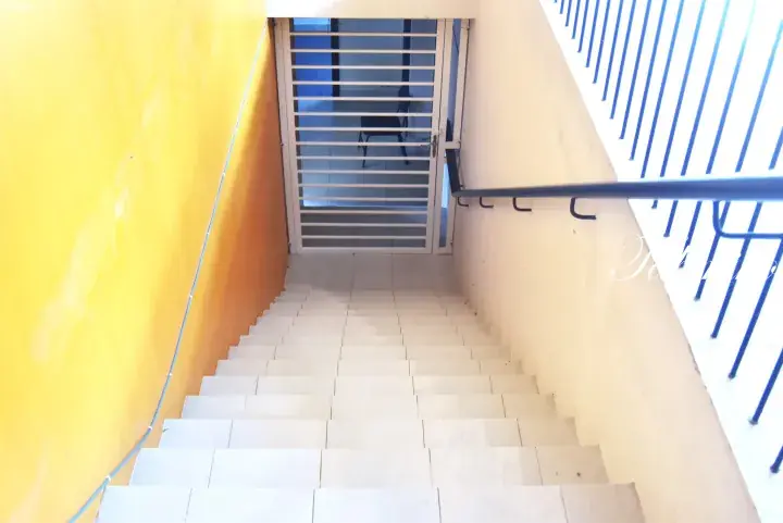 View down a tiled staircase with a yellow wall and white metal gate at the bottom.