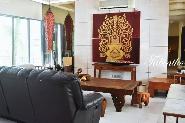 Luxury living room with a black leather sofa, wooden coffee table, and traditional Thai-style wall art.