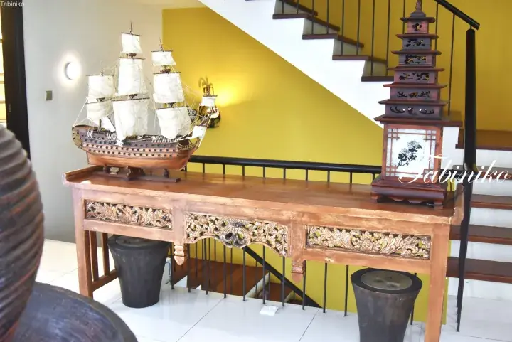 Decorative wooden console table with intricate carvings, featuring a model sailing ship and a tiered pagoda lamp in a home interior.
