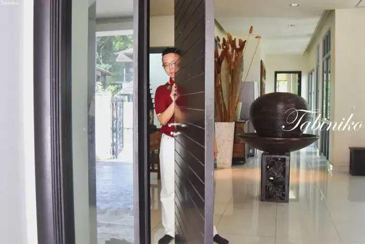 Man in red shirt opens a wooden door inside a modern villa hallway featuring a large decorative bowl.