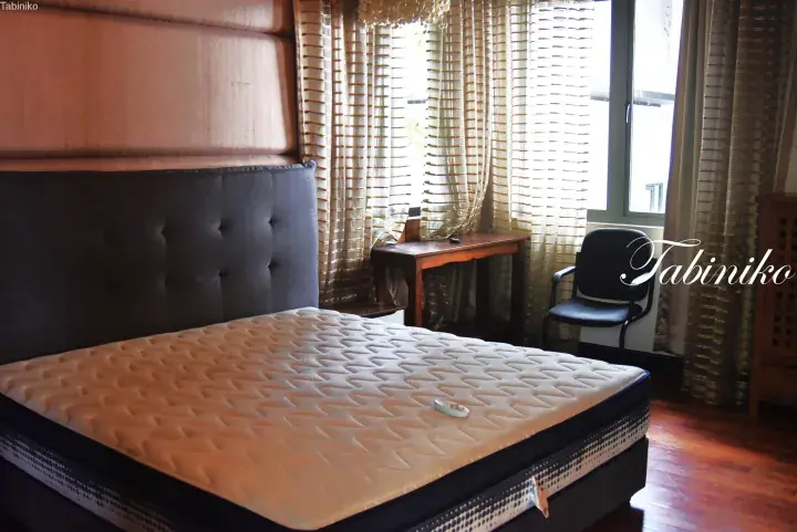 A bedroom with a large bed, tufted headboard, and window with curtains in a Malaysian property.