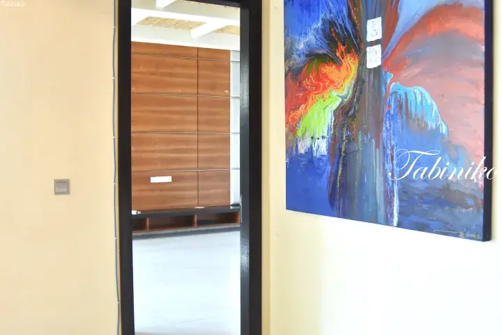 Interior view showing a doorway leading to a room with wooden cabinetry and a colorful abstract painting on the wall.