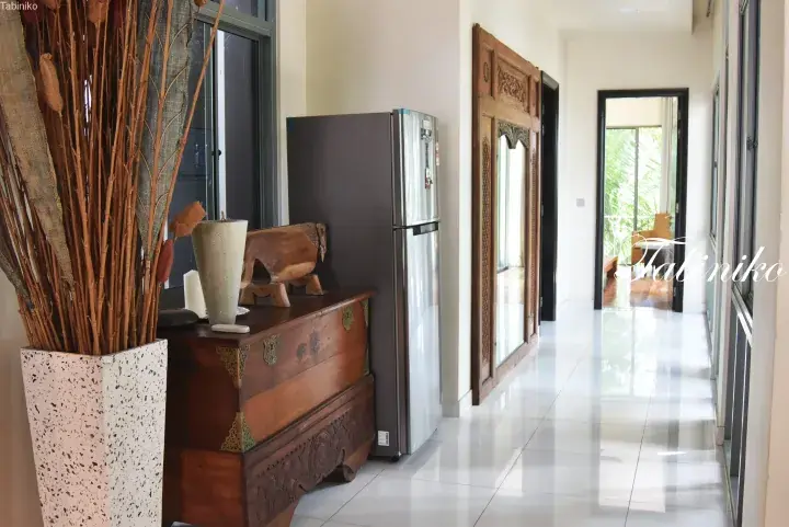 Spacious hallway with polished white tiles, a vintage wooden chest, a large planter with dried reeds, and a carved wooden door frame.
