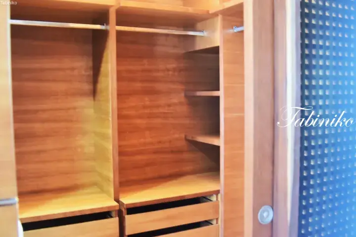 Interior of a wooden wardrobe with hanging space, shelves, and drawers, featuring a blue perforated door panel.