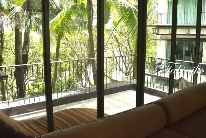 View from a balcony with a sofa, overlooking lush tropical trees and a private pool at a resort.