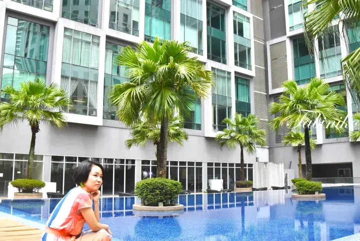 Woman relaxing by the poolside at a modern serviced residence in Malaysia, surrounded by palm trees.