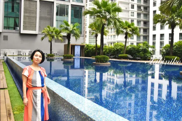 Woman in colorful dress standing by a swimming pool at a modern apartment complex in Malaysia.