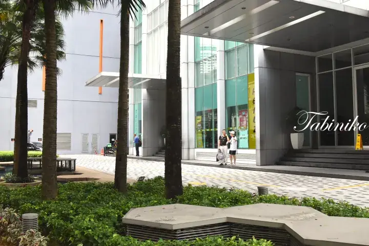 Modern building entrance with palm trees and visitors near a Hertz rental office.