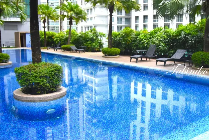Swimming pool with blue mosaic tiles, surrounded by palm trees and lounge chairs at a tropical property.