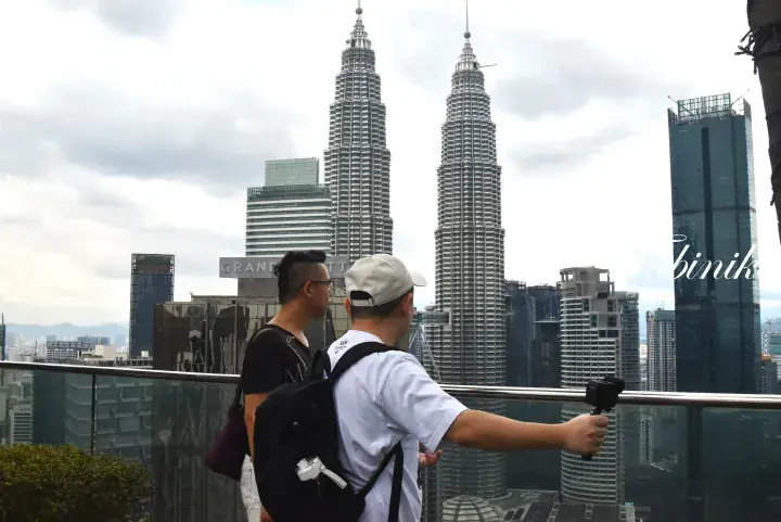 Two tourists take a selfie video with a gimbal at a rooftop view of the Petronas Twin Towers in Kuala Lumpur.
